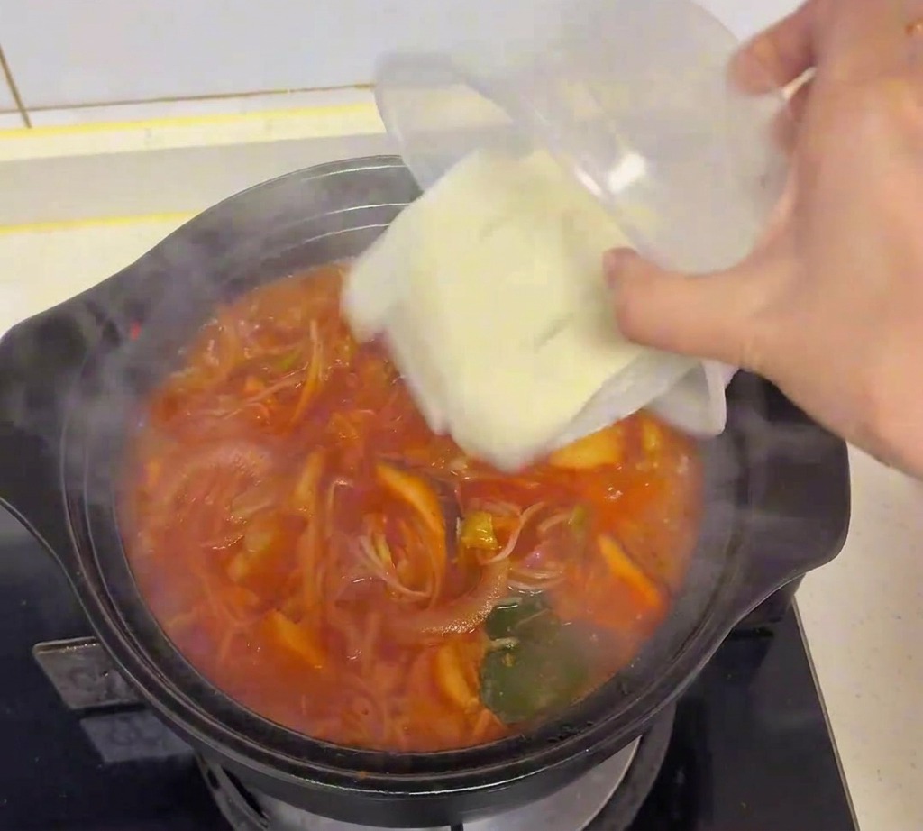 Cubos de tofu blanco fresco vertiéndose desde un recipiente de plástico a la sopa de kimchi hirviendo.