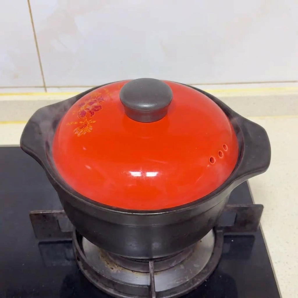 Una tapa de cerámica roja cubriendo la olla negra en la estufa con vapor escapando por el lateral.