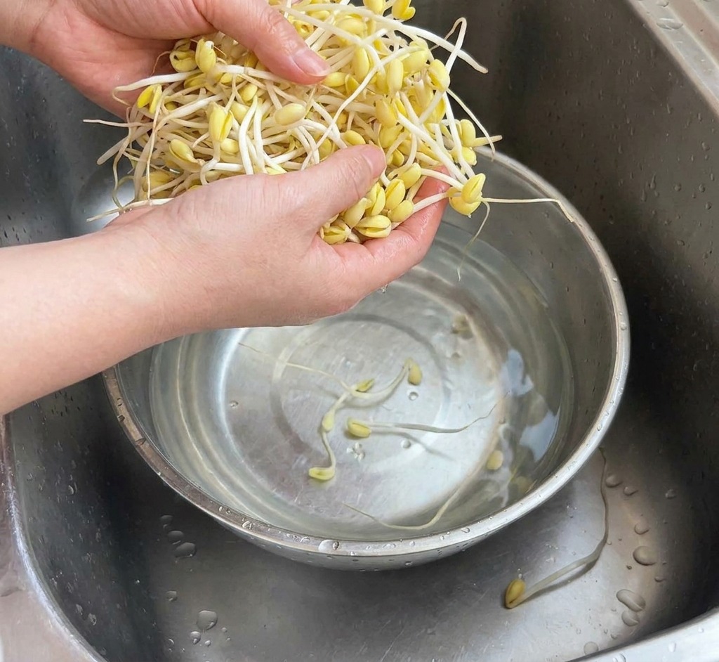 Manos lavando un manojo de brotes de soja amarilla en un bol de acero inoxidable bajo el grifo de la cocina.