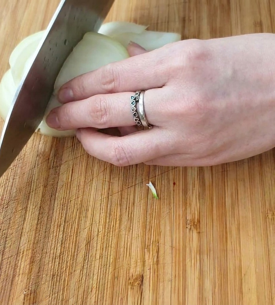 Primer plano de una mano usando un cuchillo de chef para cortar una cebolla blanca en trozos cuadrados sobre una tabla de madera.