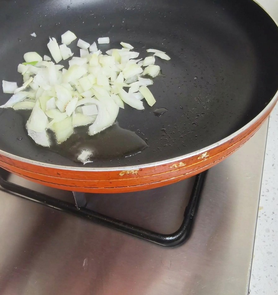 Un montón de cebolla blanca picada en una sartén antiadherente con un poco de aceite.