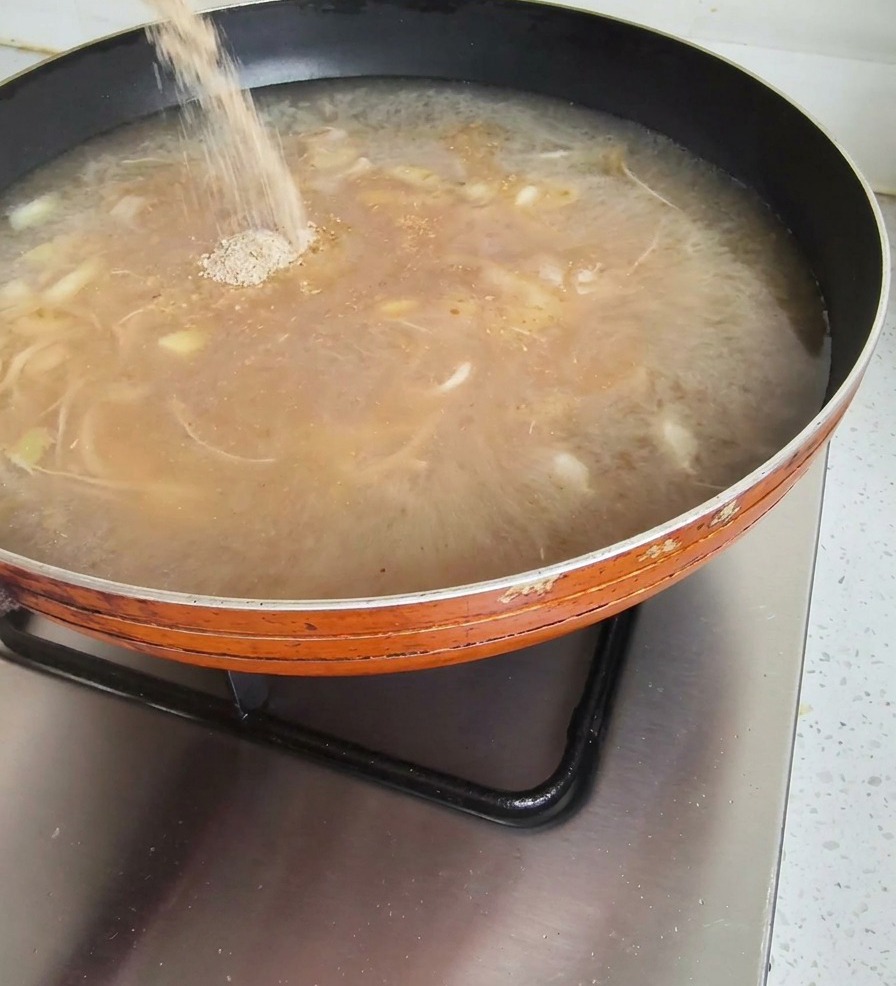 Sazonador en polvo cayendo desde un paquete a una sartén con caldo hirviendo en la cocina.