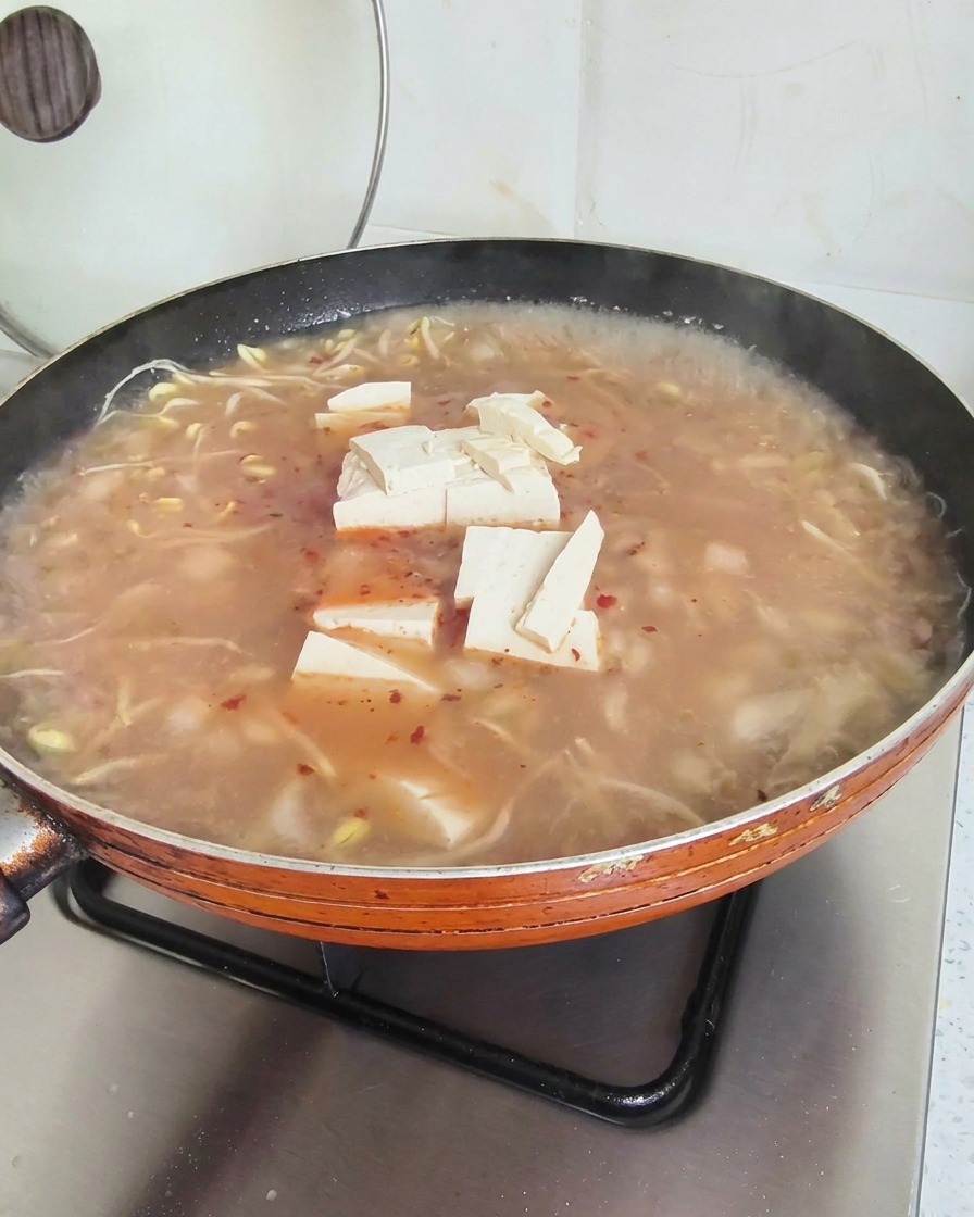 Cubos de tofu flotando en la superficie de una sopa rojiza en una sartén naranja grande.