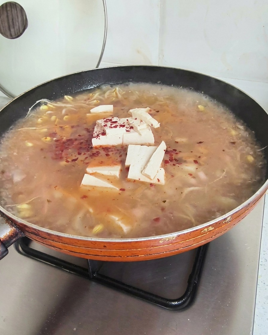 Copos de chile rojo brillante esparcidos sobre una sopa hirviendo con tofu y brotes de soja.
