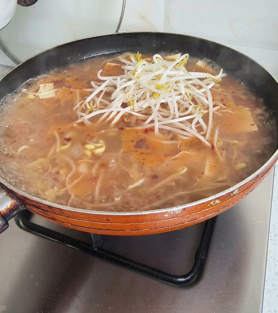 Un montón de brotes de soja frescos colocados sobre una sartén de sopa hirviendo.