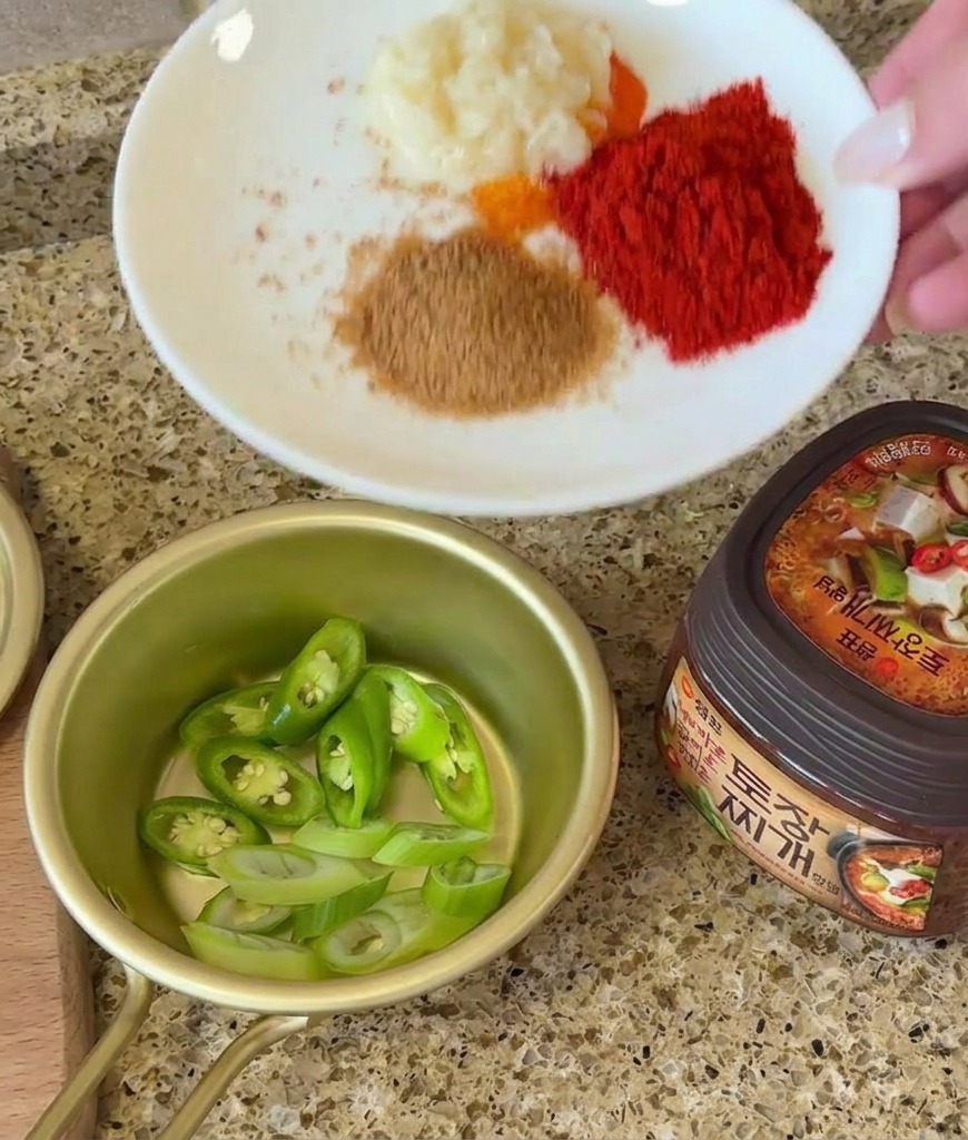 Una mano sosteniendo un plato con ajo y especias junto a chiles cortados y pasta de soja.