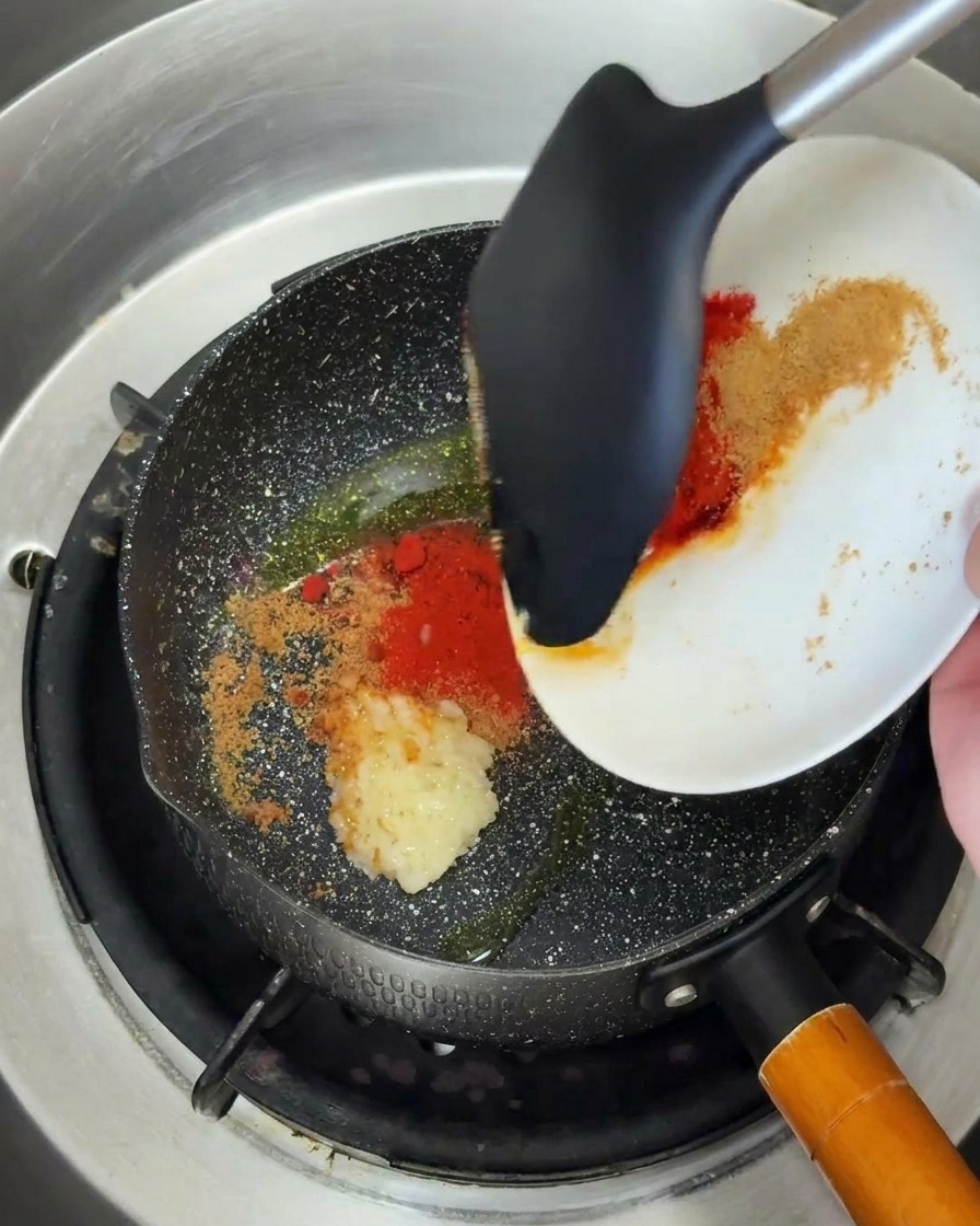 Ajo picado y chile en polvo siendo añadidos a una sartén caliente con aceite.