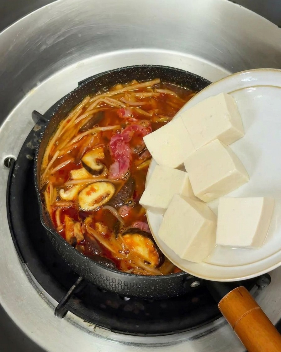 Cubos de tofu blanco fresco pasando de un plato a la olla de sopa coreana.