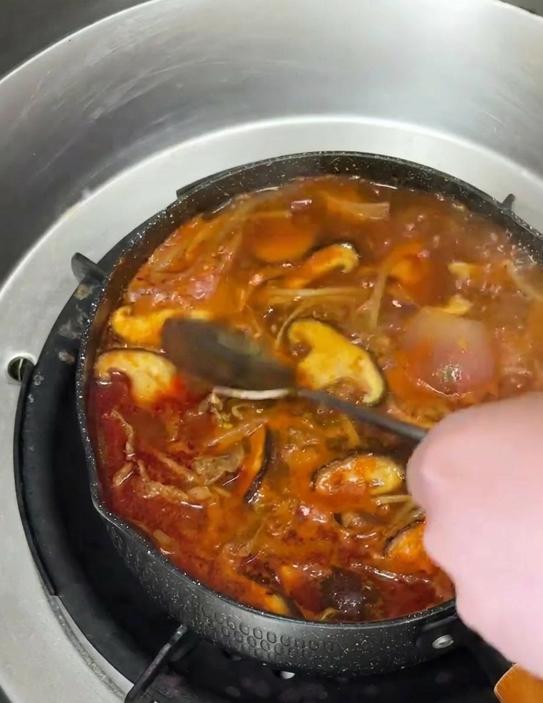 Una cuchara vertiendo aceite de sésamo ámbar sobre la sopa coreana picante.