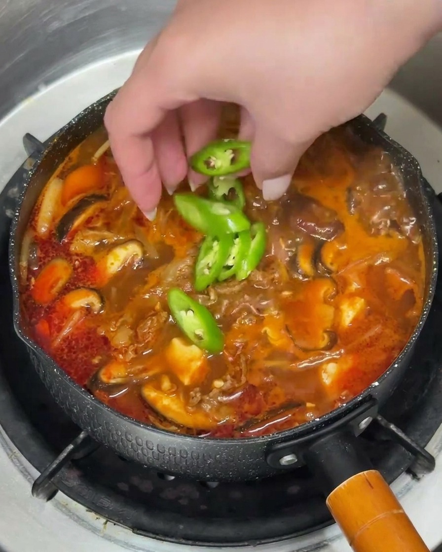 Una mano esparciendo aros de chile verde y cebolleta picada sobre la sopa humeante.