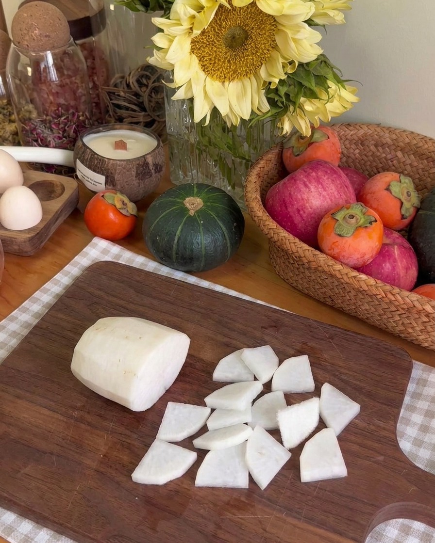 Trozos de nabo blanco cortados finamente dispuestos en una tabla de madera junto a un trozo más grande de nabo crudo.