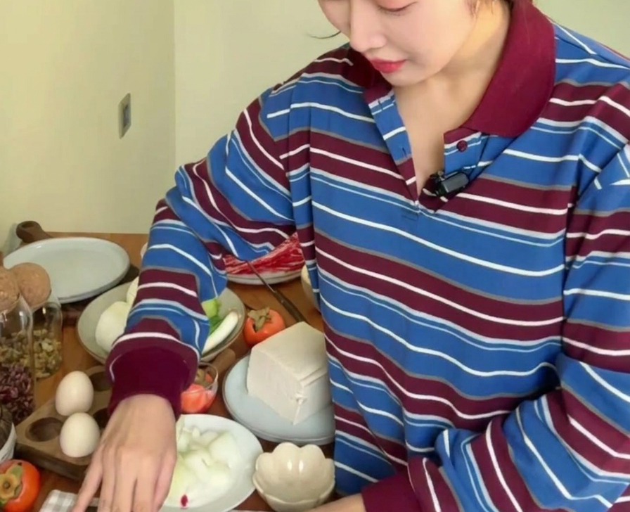 Una persona usando un cuchillo de cocina para picar finamente dientes de ajo frescos sobre una superficie de madera rodeada de otras verduras.