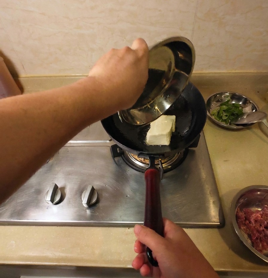 Un bloque sólido de tofu blanco añadiéndose a un wok con aceite caliente para comenzar el proceso de fritura.