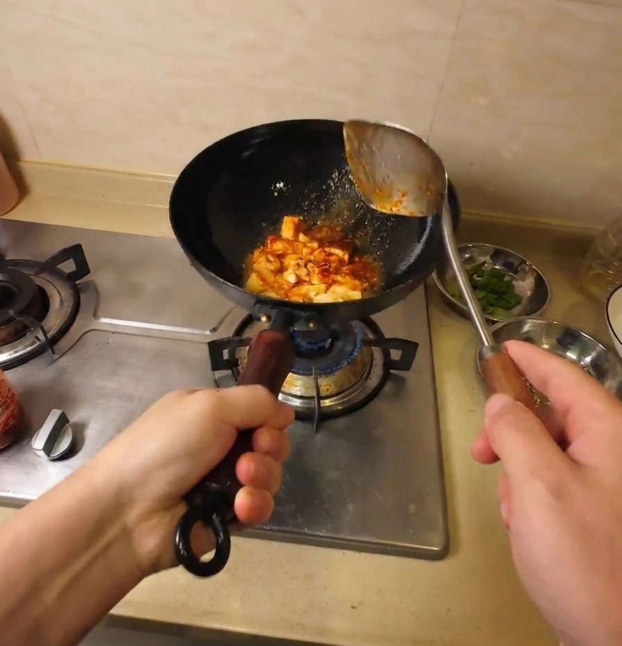 Trozos de tofu siendo salteados y cubiertos con una salsa roja sabrosa en un wok negro.