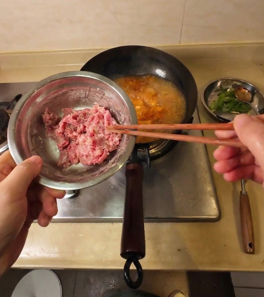 Una mano usando palillos para levantar láminas de ternera cruda cubiertas de almidón sobre una olla de sopa hirviendo.