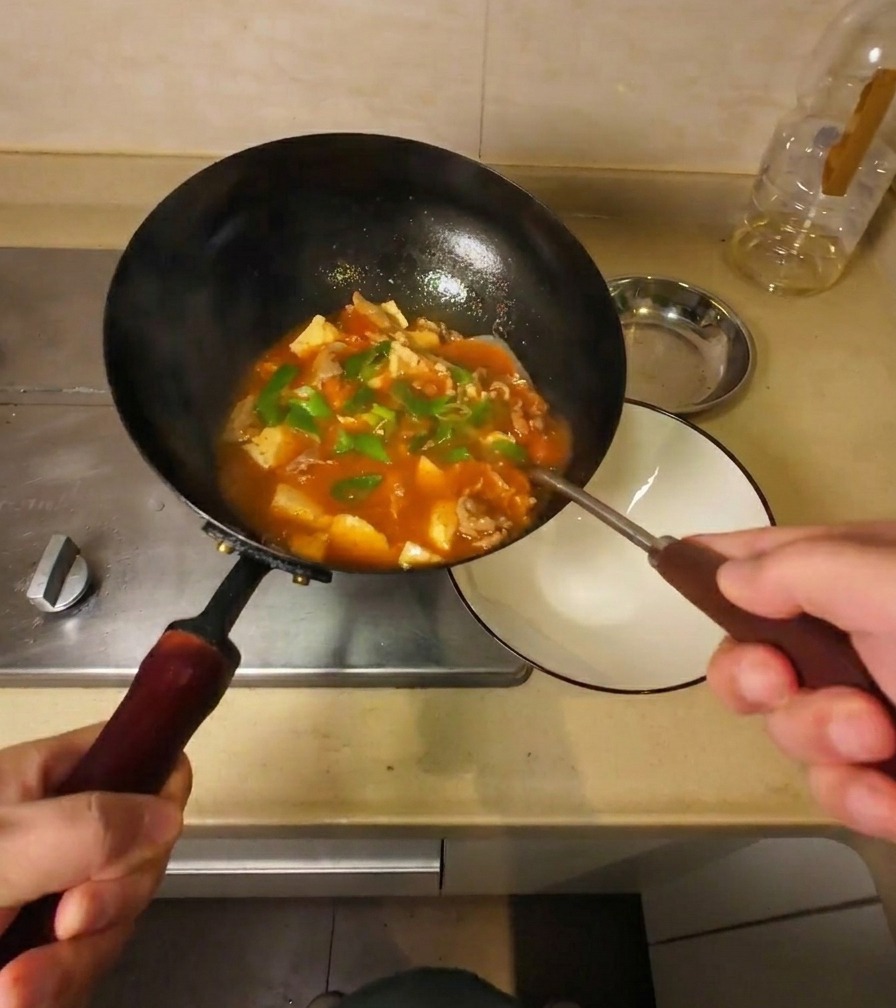 La sopa de ternera y tofu terminada vertiéndose desde un wok negro en un cuenco de cerámica blanca para servir.