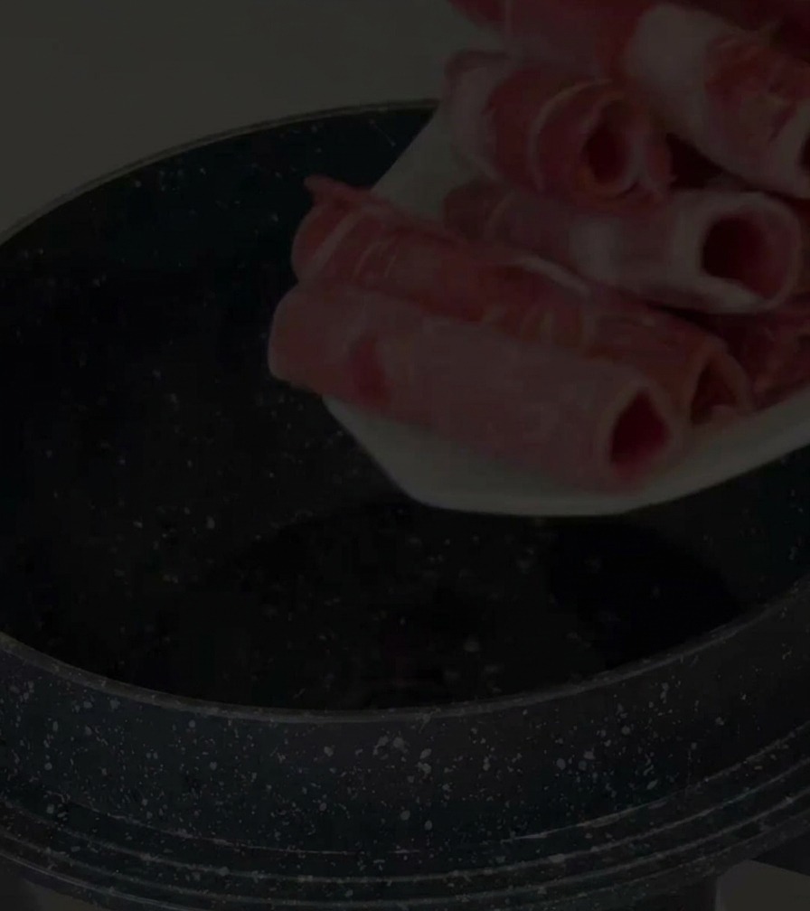 Una mano colocando láminas finas de falda de ternera cruda en una olla antiadherente negra.