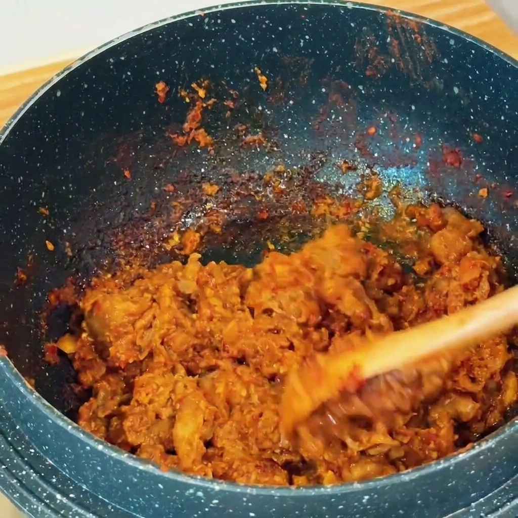 Ternera laminada salteándose con pasta de soja marrón rojiza en una olla oscura con una espátula de madera.