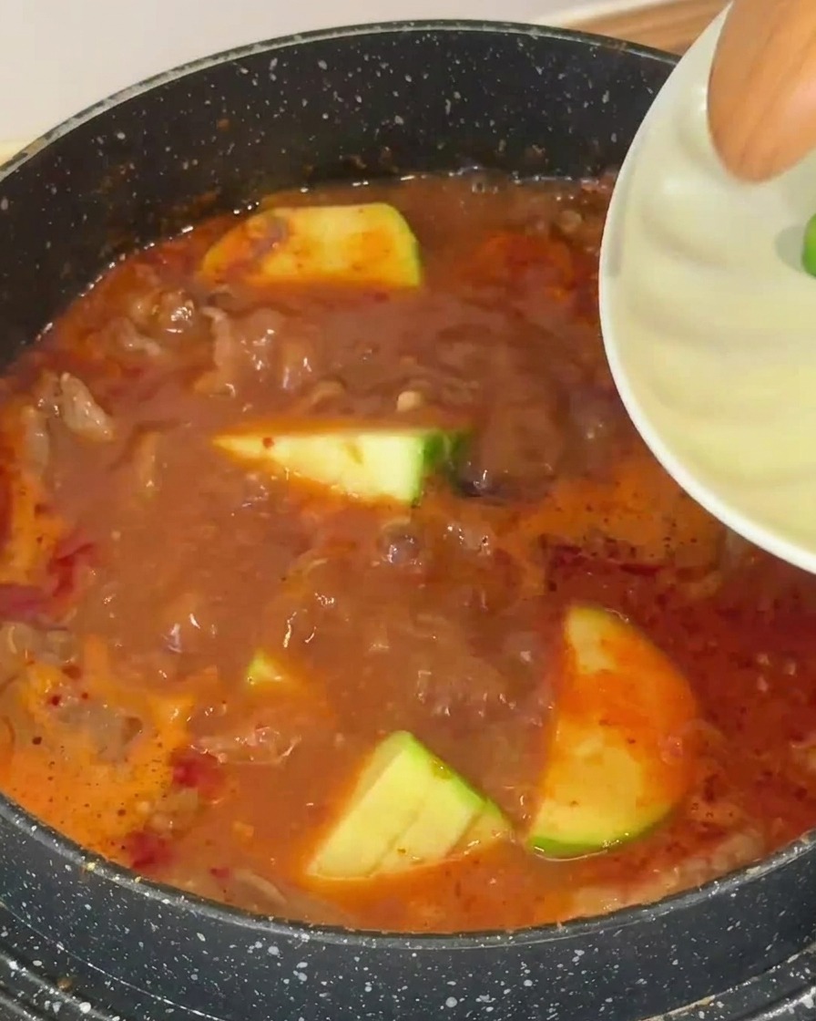 Rodajas de calabacín verde cayendo en un caldo de sopa rojizo que hierve.