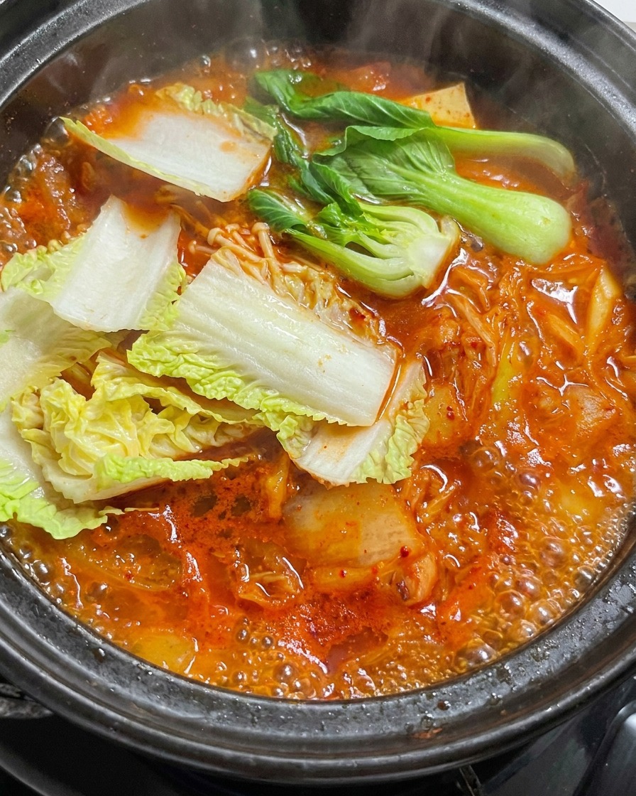Hojas de col frescas añadiéndose a un estofado rojo burbujeante en una olla de piedra.