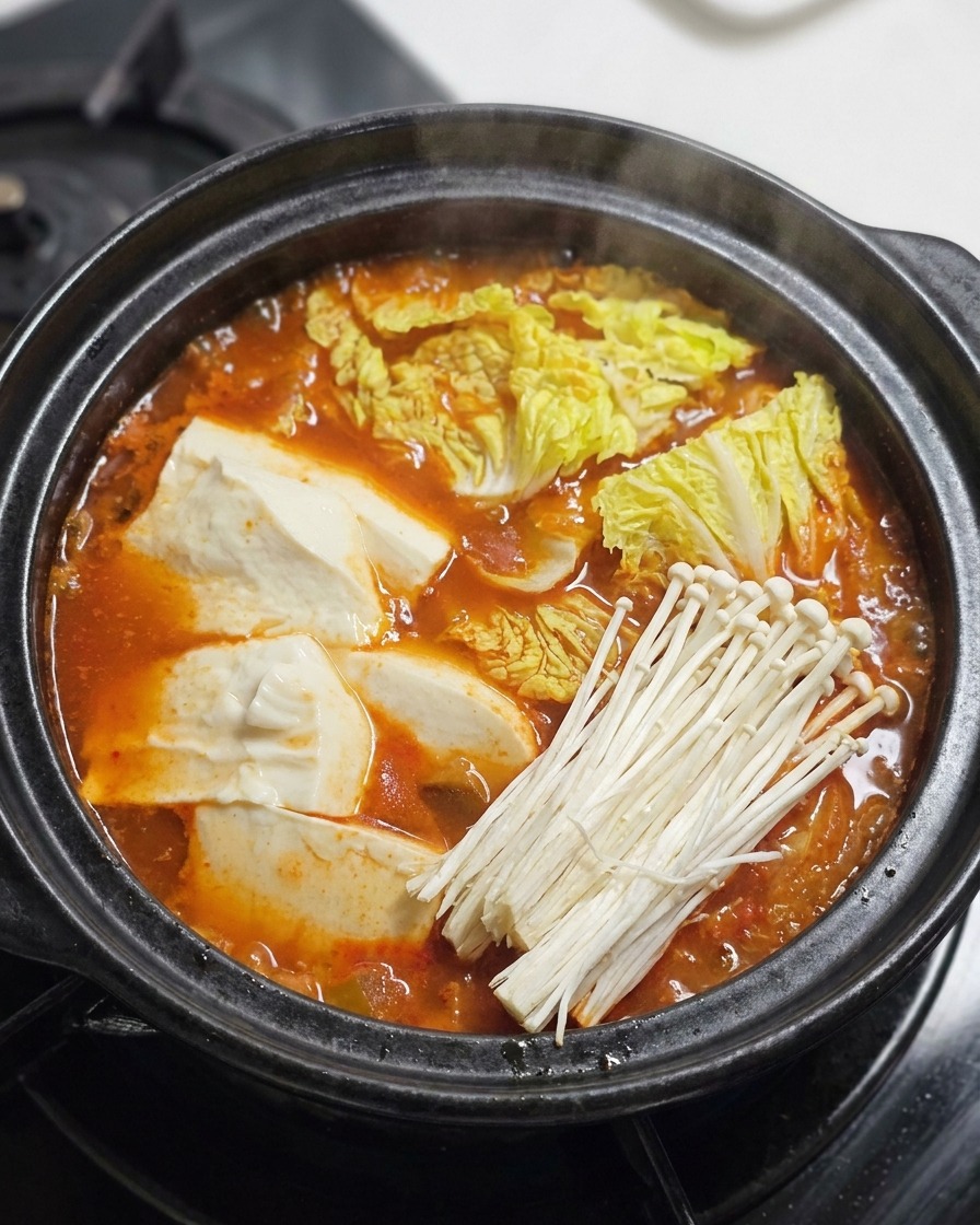 Ternera sellada, champiñones enoki y cebolleta verde añadiéndose a la parte superior de un estofado rojo burbujeante.