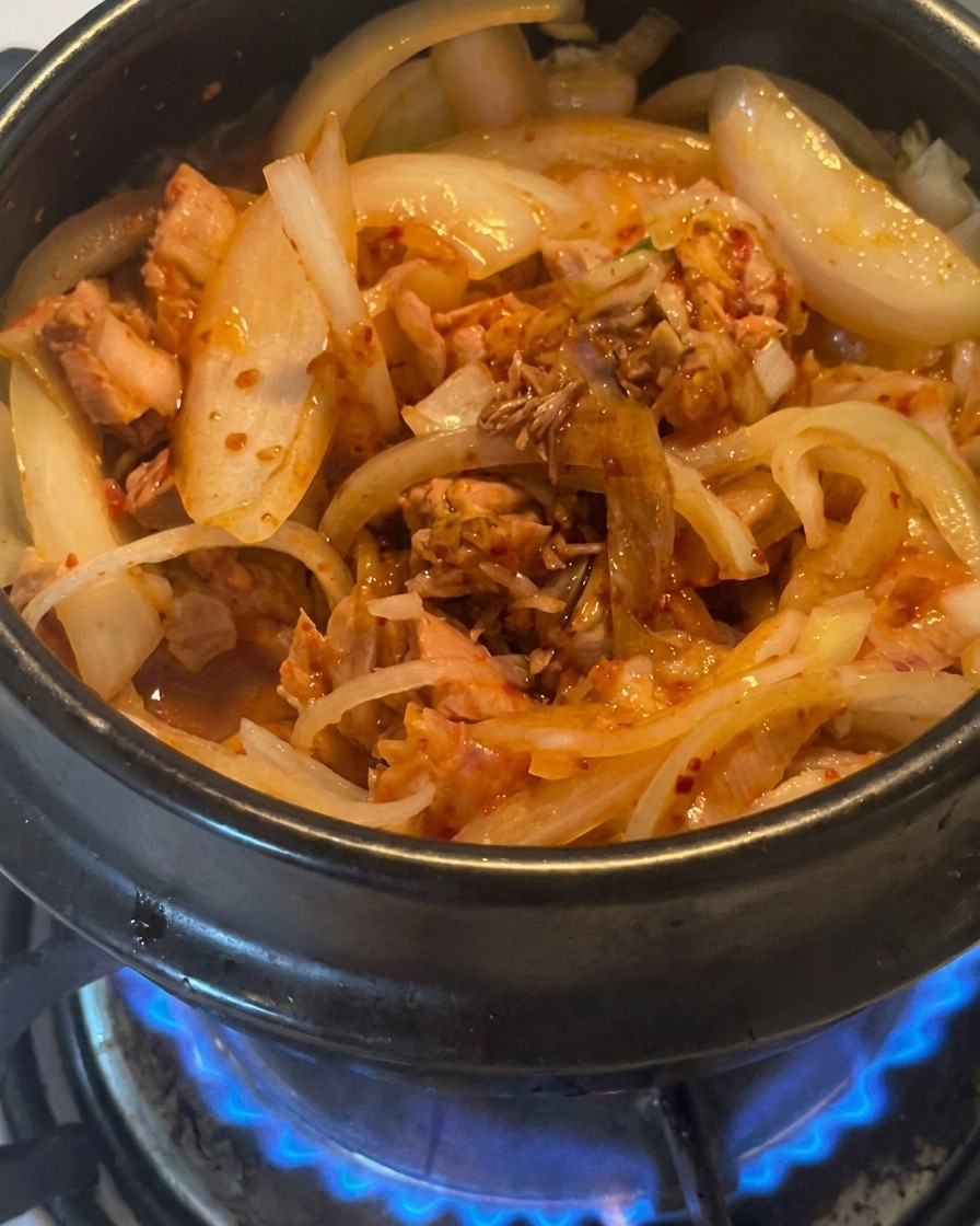 Primer plano de salsa de soja oscura cayendo sobre la mezcla de atún, kimchi y cebollas en la olla.