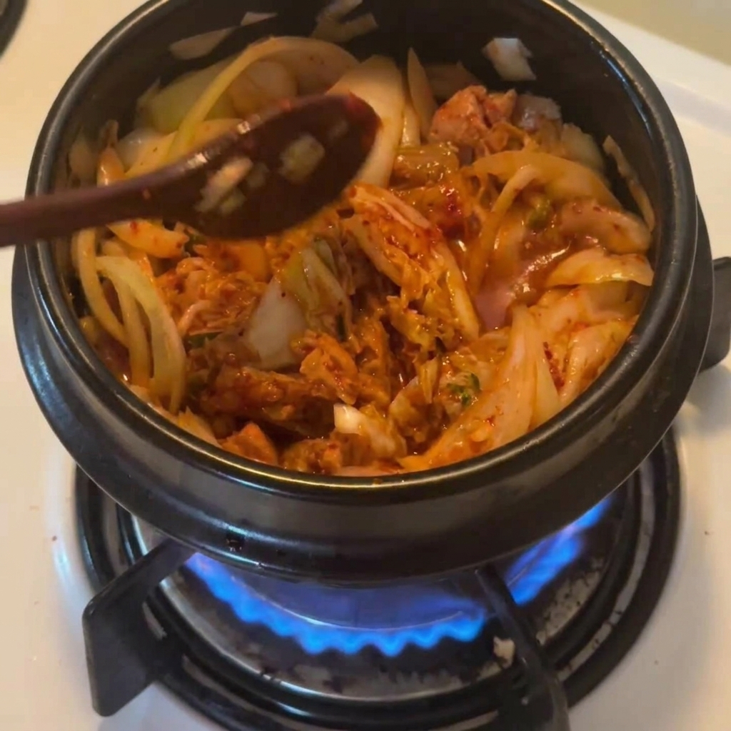 Cuchara de madera espolvoreando chile en polvo coreano rojo sobre el guiso en la olla negra.