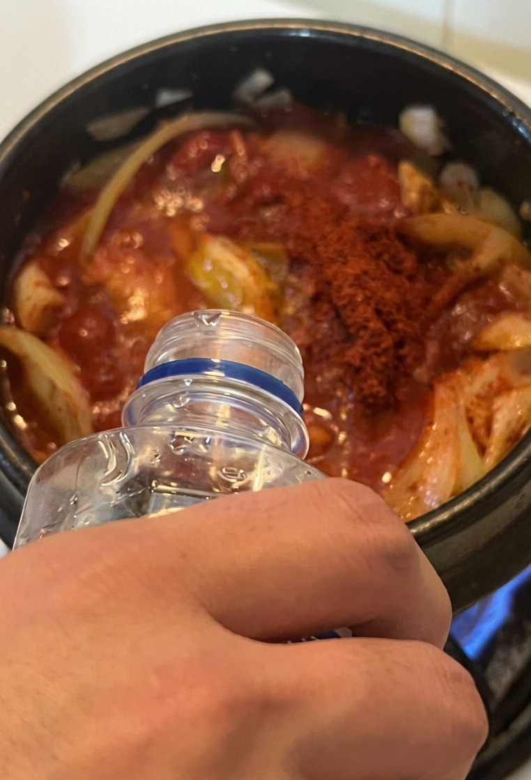 Agua vertiéndose desde una botella transparente en la olla de estofado rojo sobre la estufa.