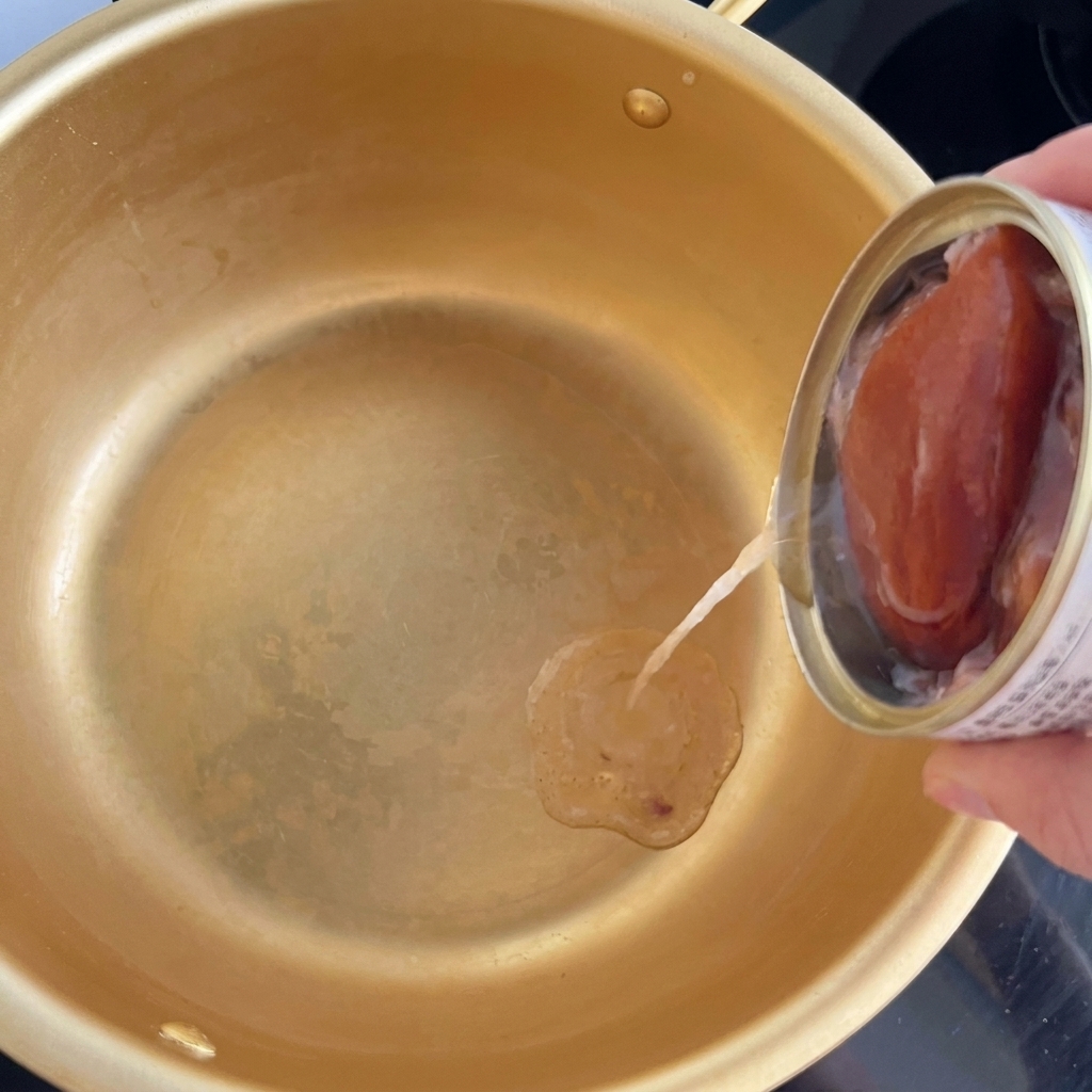 Aceite de una lata de atún vertiéndose en una olla dorada tradicional coreana.
