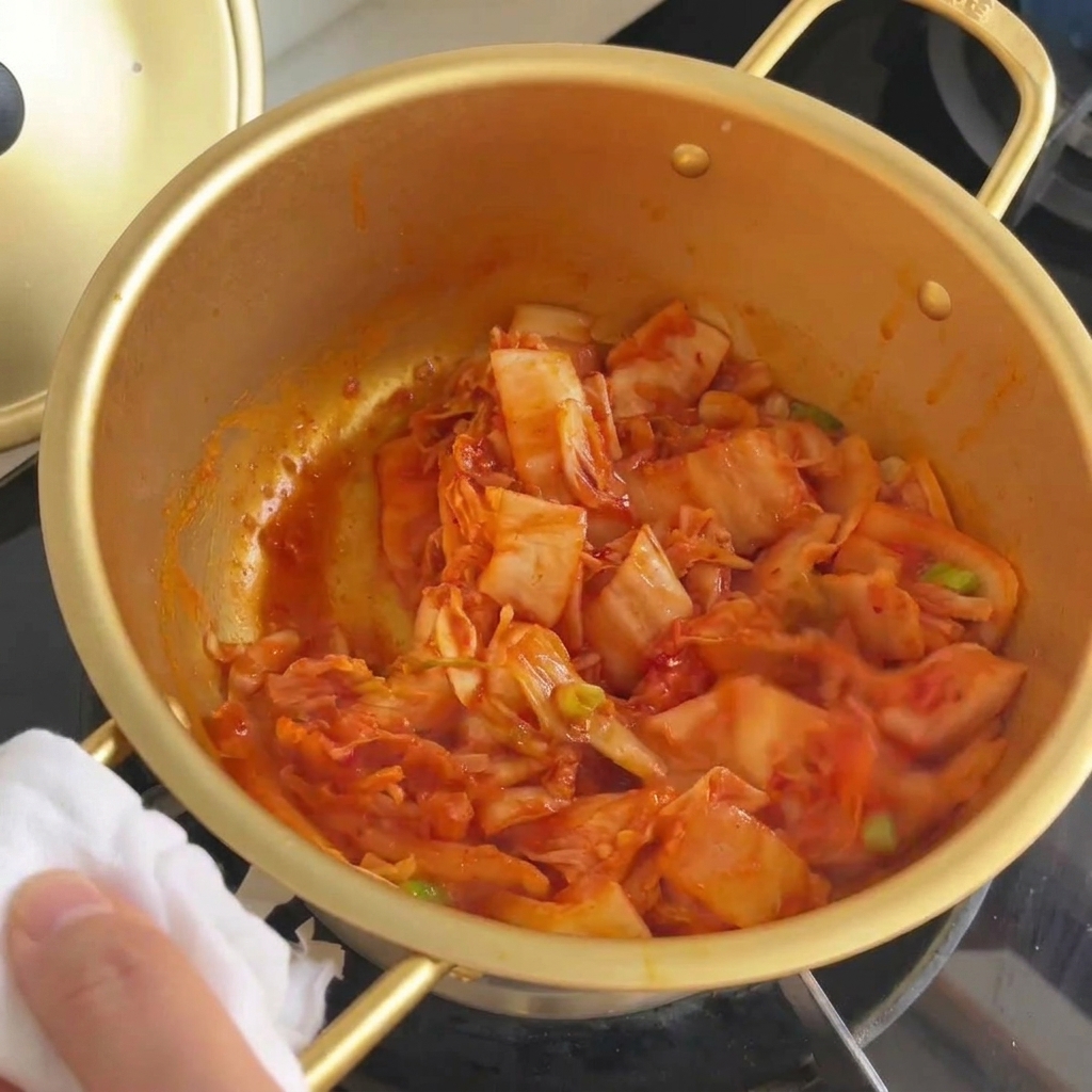 Kimchi y cebolletas mezclándose en la olla hasta que la col se ve translúcida.