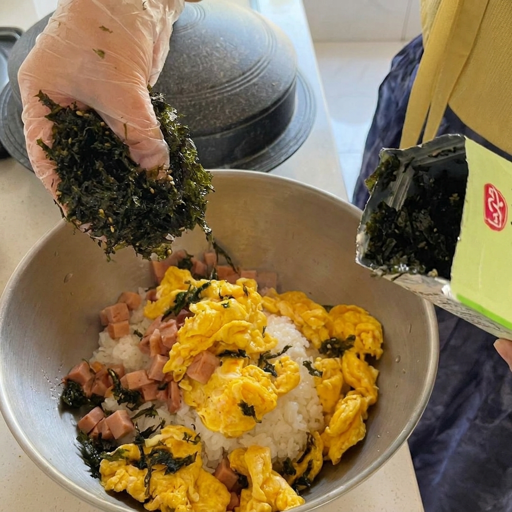 Trozos grandes de atún en conserva añadiéndose al estofado de kimchi rojo burbujeante.