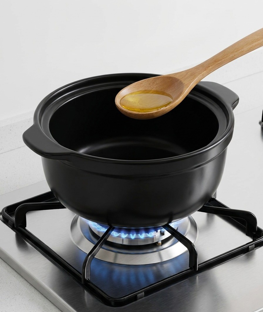 Aceite de sésamo dorado vertido en el fondo de una olla de cerámica negra sobre el fuego.