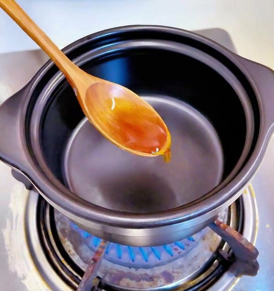 Cuchara de madera removiendo ajo picado en aceite en el fondo de una olla negra.