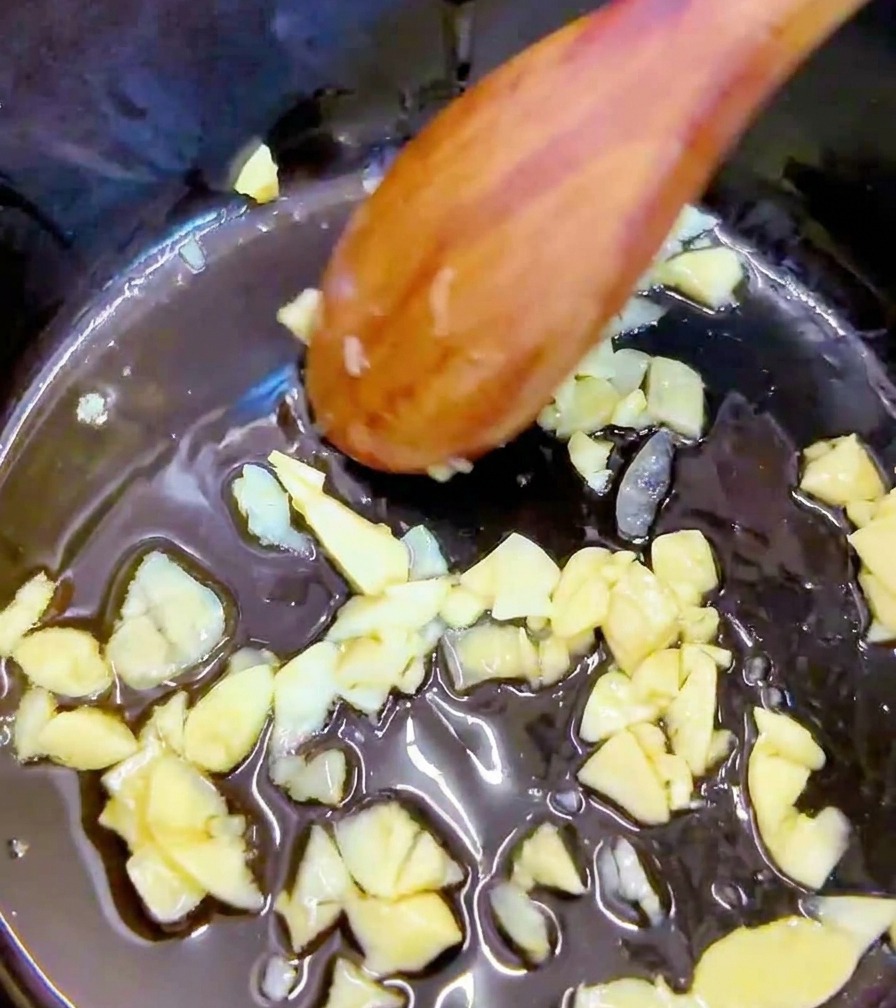 Trozos de kimchi rojo picante siendo mezclados con ajo en una olla con una cuchara de madera.