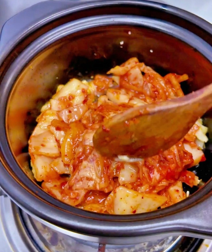 El líquido de una lata de atún vertido sobre la mezcla de kimchi y ajo en una olla negra.
