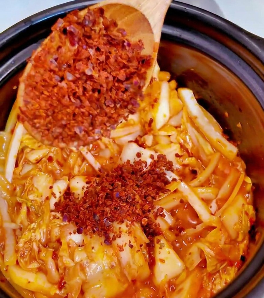 Añadiendo una cucharada de chile rojo en polvo fino a la olla con el kimchi y los aromáticos.