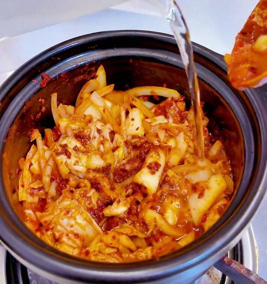 Agua vertida desde un recipiente en una olla negra llena con la base de kimchi picante.