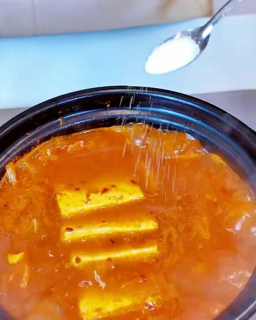 Sal blanca espolvoreada desde una cuchara pequeña sobre la superficie de una sopa roja.