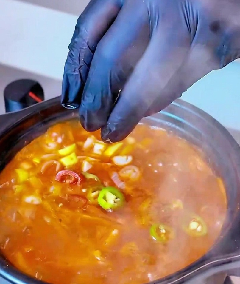 Rodajas de chile rojo y verde cayendo en una olla de Sopa de Kimchi con Atún como toque final.