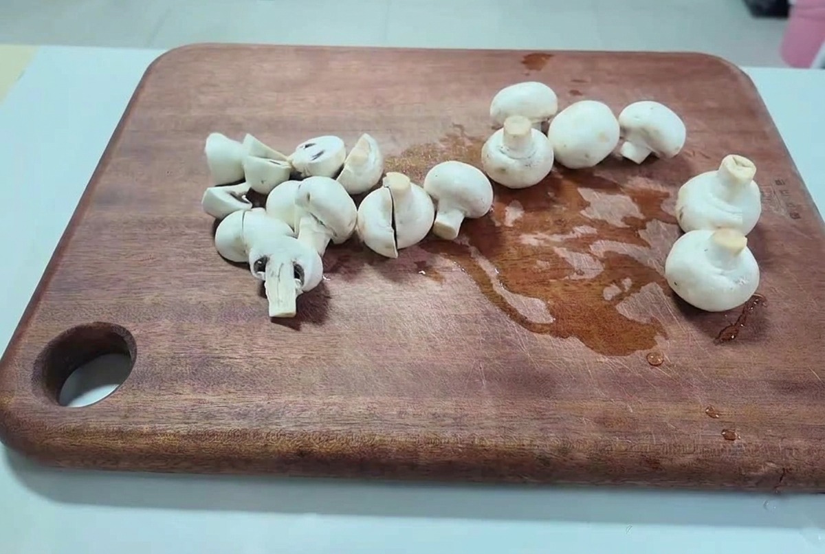 Champiñones frescos cortados por la mitad y en trozos gruesos sobre una tabla de cortar de madera oscura.