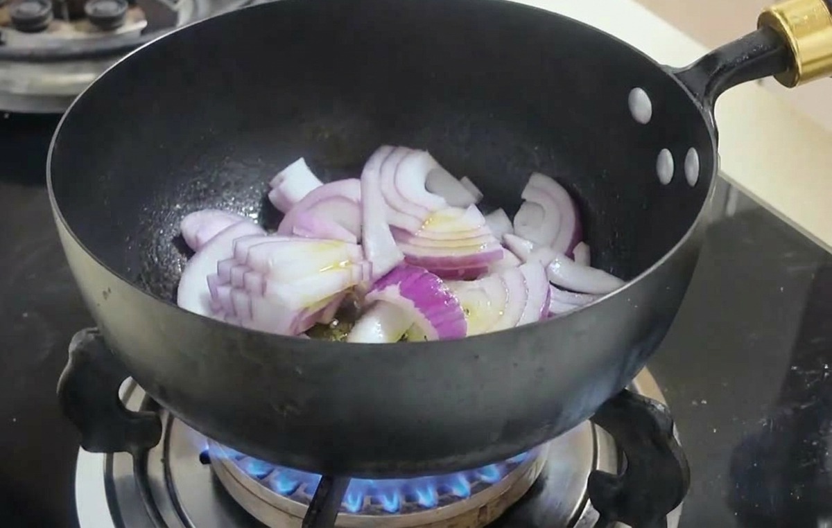Gajos de cebolla roja salteándose en un wok negro sobre una llama de gas azul.