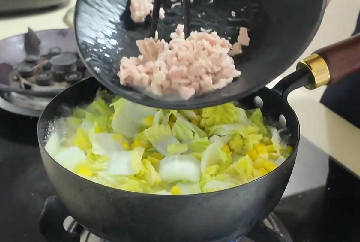 Atún desmigado siendo añadido con palillos a una sopa de verduras que hierve.