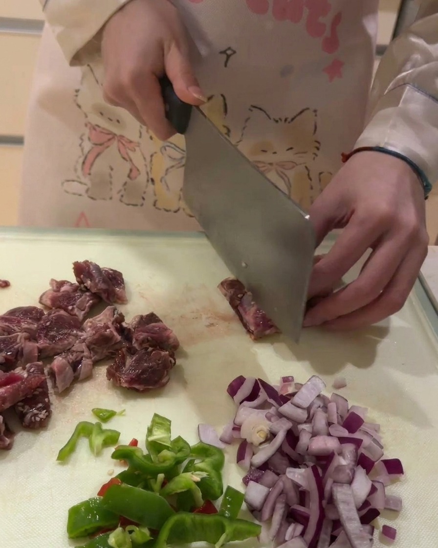 Un primer plano de carne cruda de costilla de ternera siendo cortada en pequeños dados en una tabla de cortar blanca.
