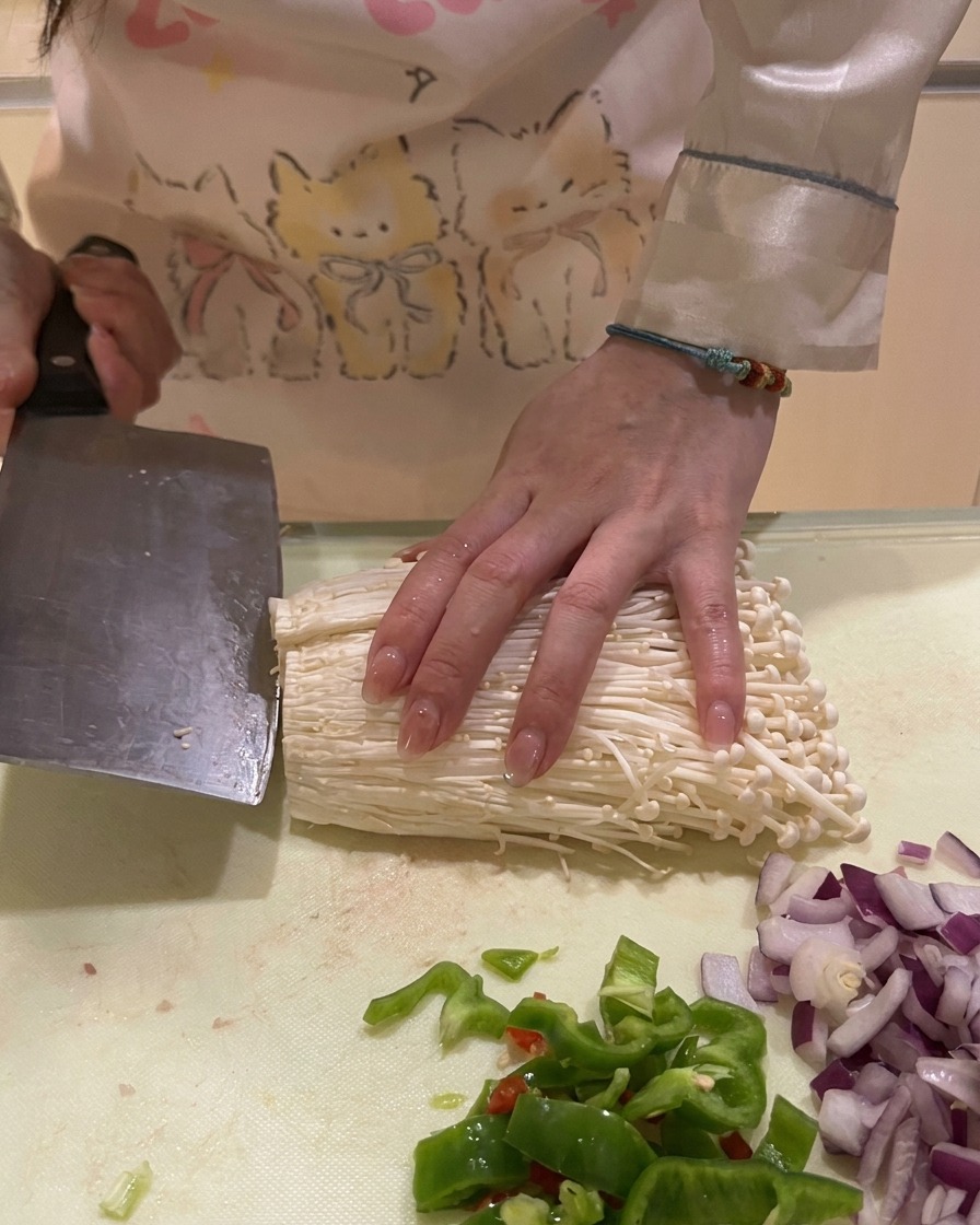 Cortando las raíces inferiores de un manojo de setas enoki blancas sobre una encimera de cocina.