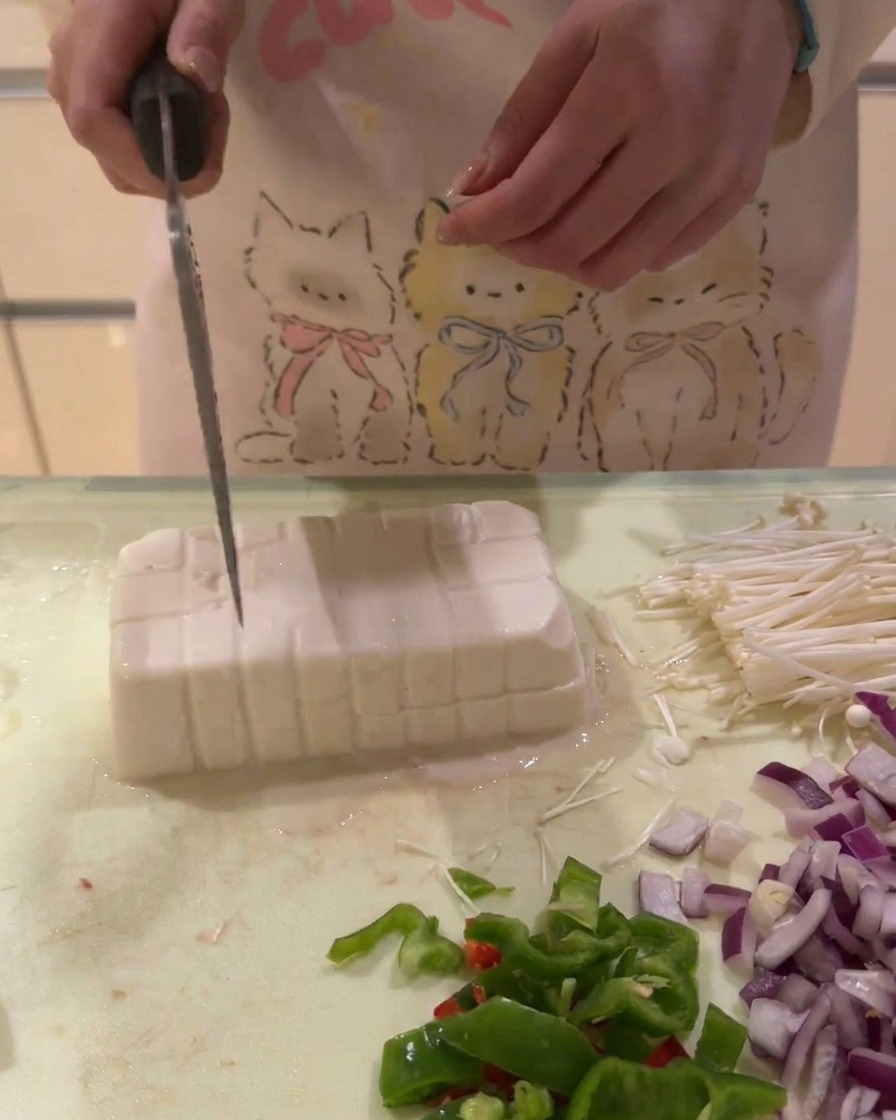 Un bloque de tofu blanco siendo cortado en una cuadrícula de pequeños dados en una tabla de cortar.