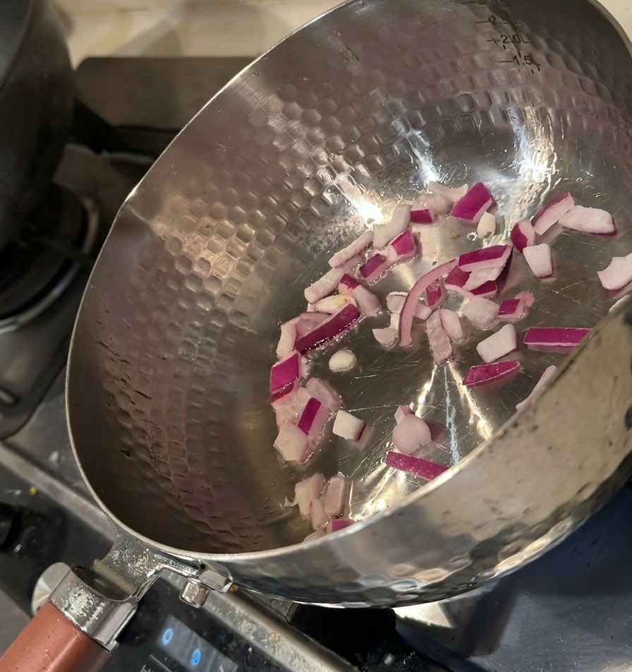 Cebolla morada picada sofriéndose en una olla de metal caliente con una ligera capa de aceite.