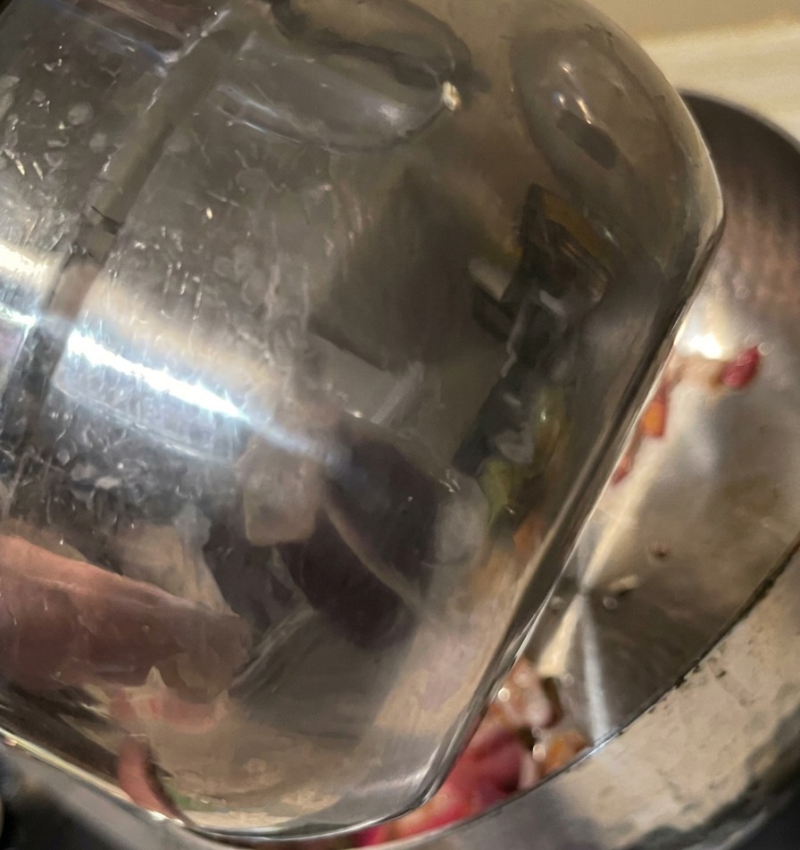Agua vertiéndose desde una jarra de acero inoxidable en una olla con cebolla morada pochada.