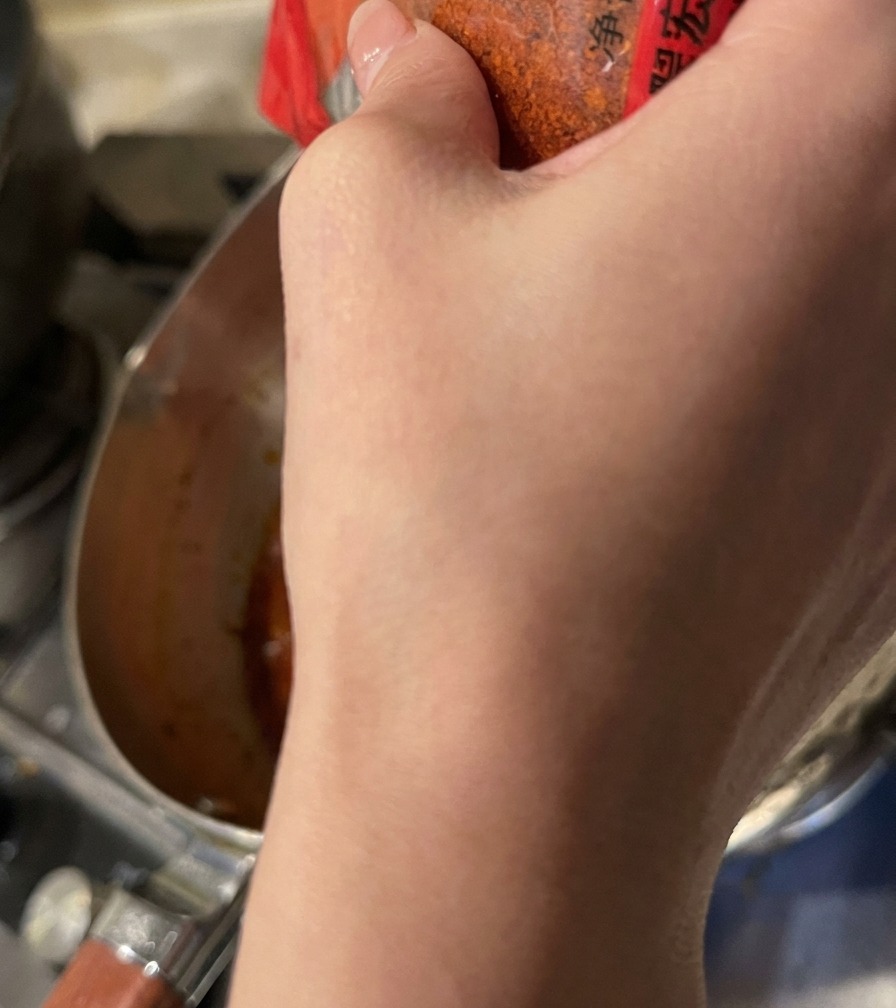 Polvo de chile rojo espolvoreándose desde un recipiente sobre la base naranja de sopa a fuego lento.