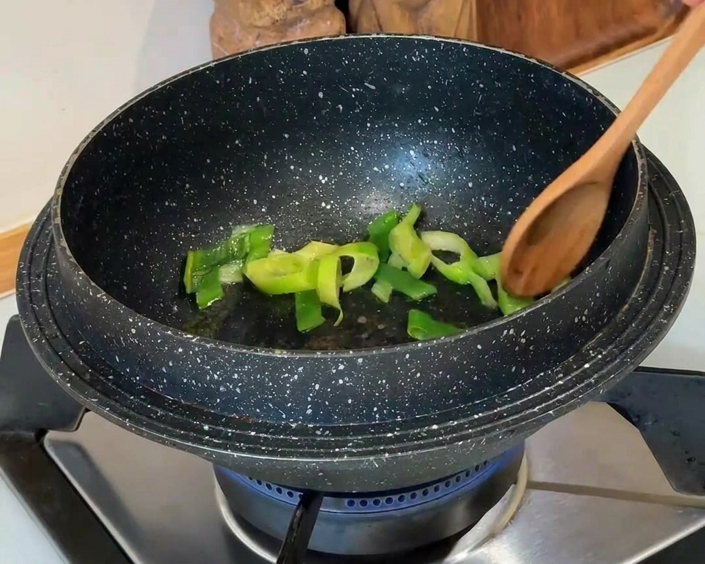 Cebolletas verdes picadas siendo removidas con una cuchara de madera en una olla de granito oscuro.