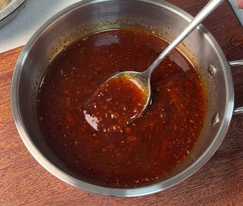 Una persona removiendo una salsa roja espesa y vibrante en un pequeño bol de acero con una cuchara de metal.